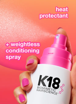 Protector de calor K18 y spray acondicionador con una mano sosteniendo la botella sobre un fondo rosa