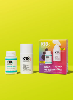 Una imagen de producto que muestra dos botellas de productos para el cuidado del cabello con una caja rosa y amarilla de fondo. Los productos están etiquetados con la marca K18.